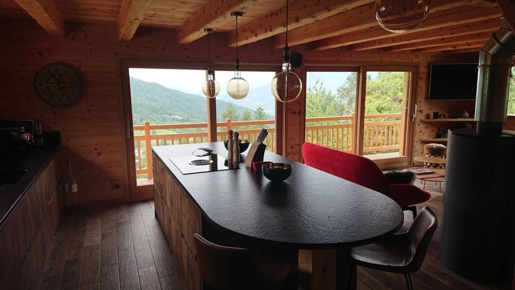 Cuisine sur mesure en bois massif avec îlot central et plan de travail en pierre noire dans chalet de montagne