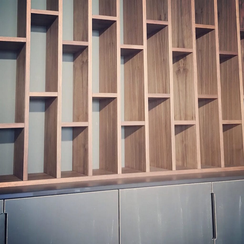 Bibliothèque avec montant verticaux étroits en bois massif sur meuble bas gris.