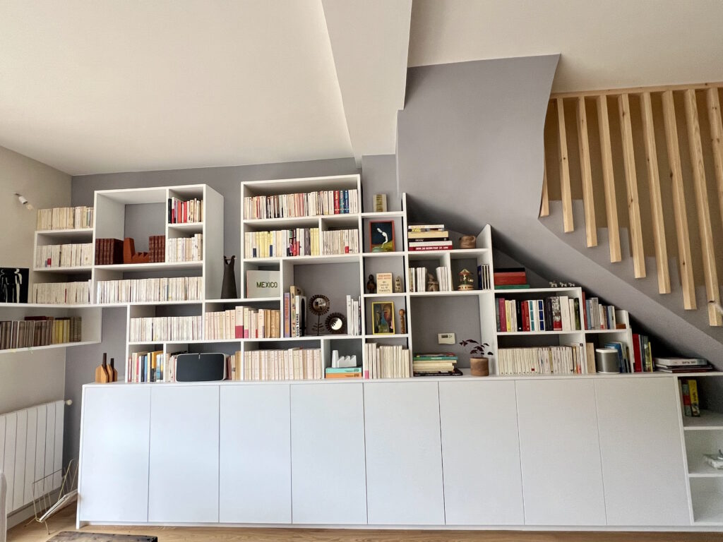 bibliotheque_sous_escalier_remplie Bibliothèque sur mesure blanc laqué asymétrique remplie de livres sous escalier.