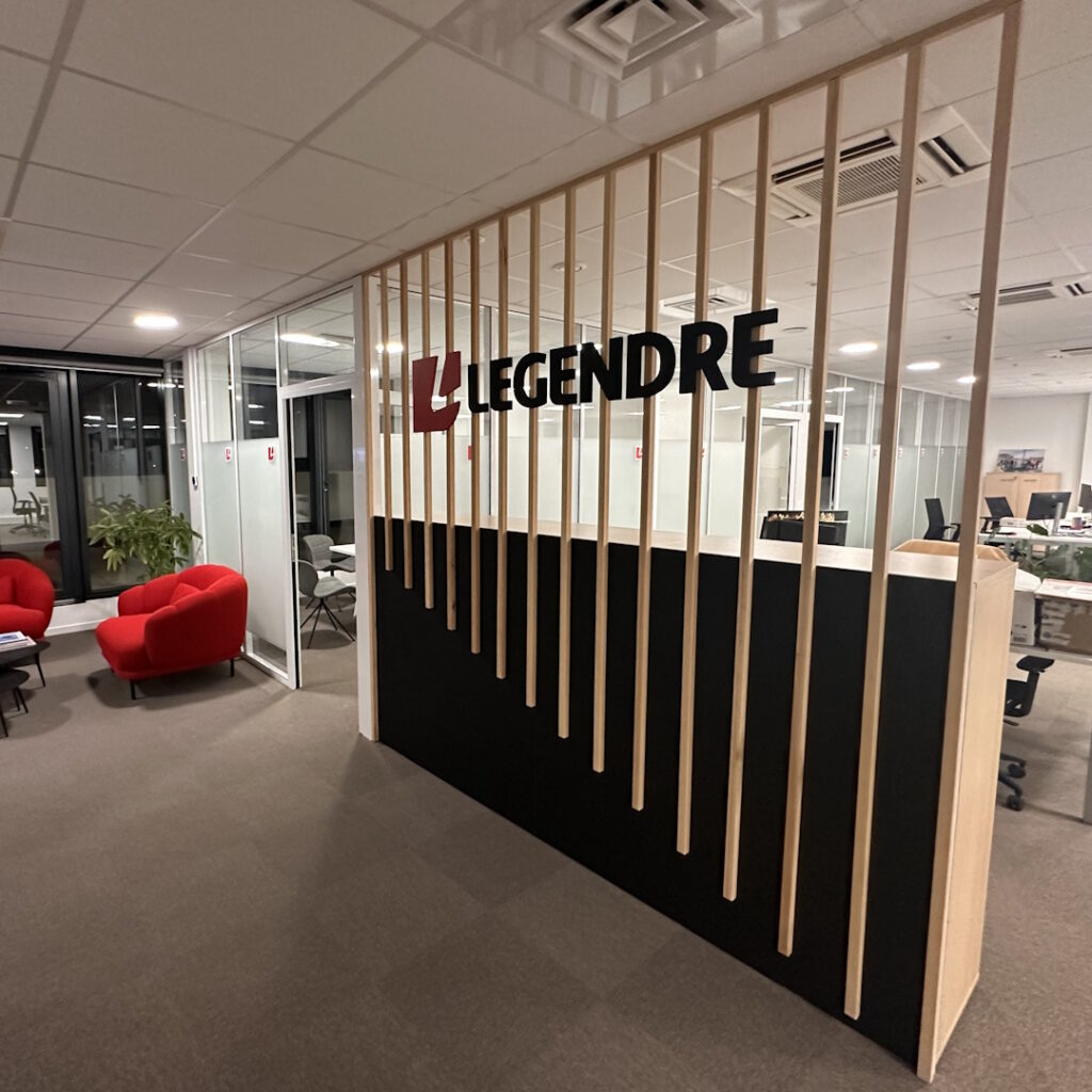 claustra-legendre Claustra de menuiserie en tasseaux de bois clair avec logo LEGENDRE, dans un accueil de bureau moderne.