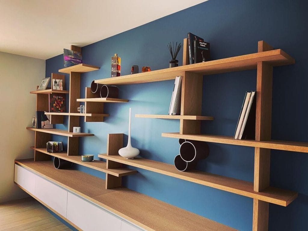 Bibliothèque murale moderne en bois clair avec étagères déstructurées sur fond bleu.