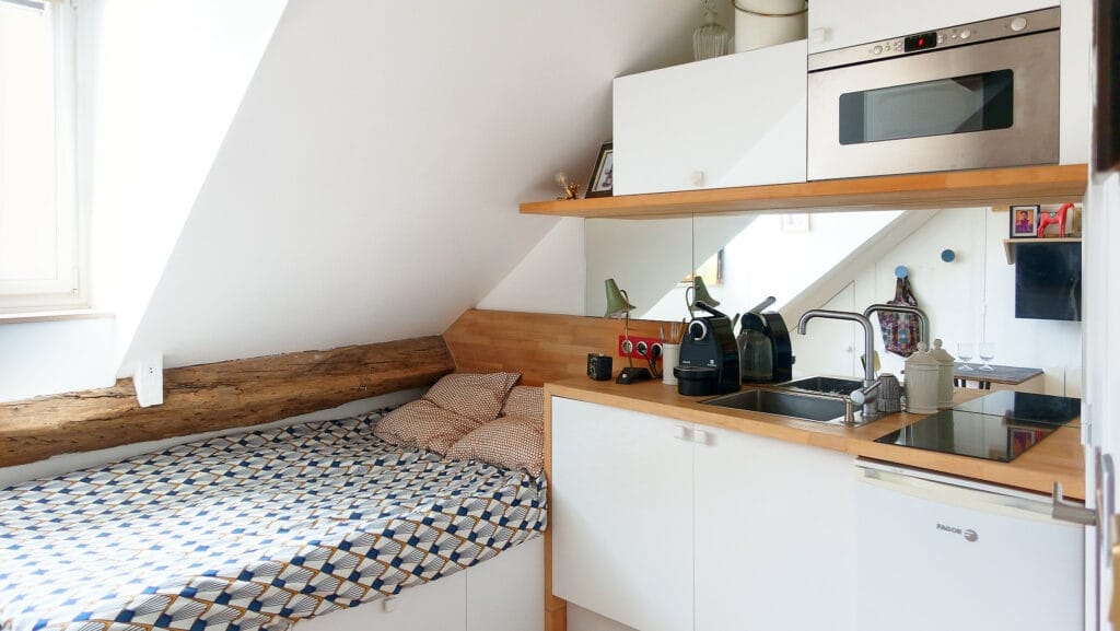 Aménagement de studio sous combles avec lit et kitchenette en bois et blanc
