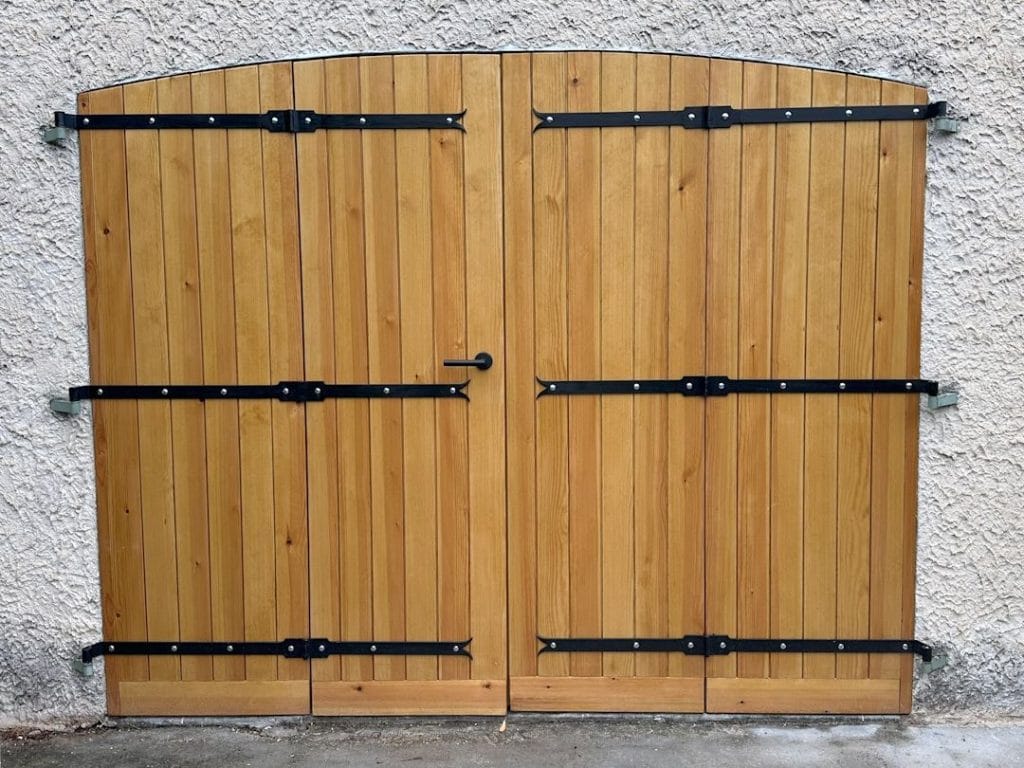 Porte de garage en bois lasurée à quartes battants avec ferronnerie noire.