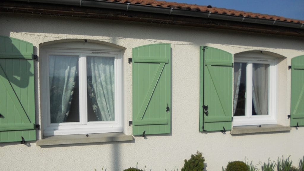 vollet_bois_arrondi Volets battants en bois vert clair installés sur fenêtres arrondies en façade de maison